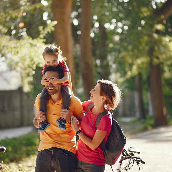 Un homme et une femme portent un enfant sur leurs épaules, souriant pendant leurs vacances en famille.